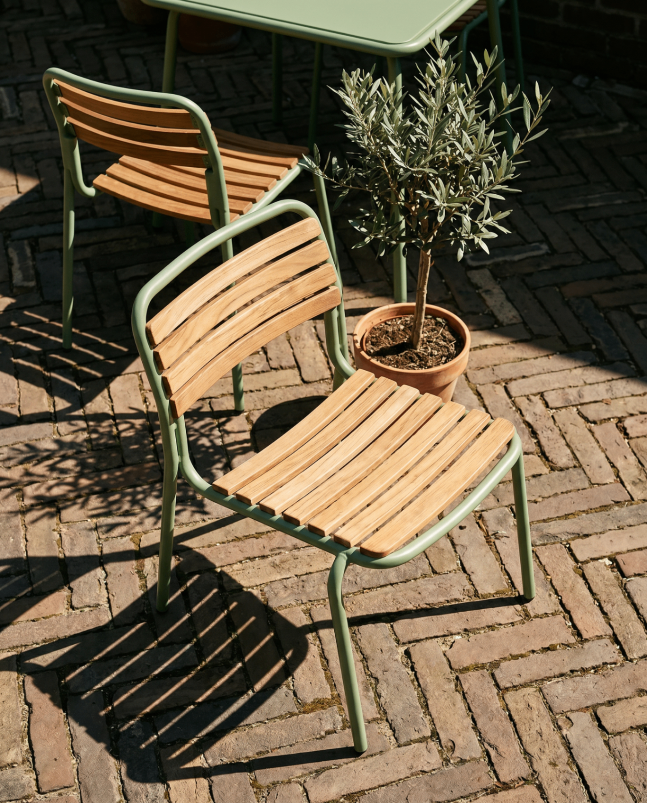 Sage-green outdoor dining chairs on a cobblestone terrace