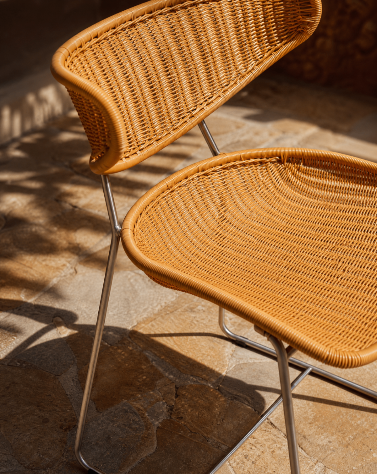 Woven rattan dining chair with stainless steel sled base on a stone patio