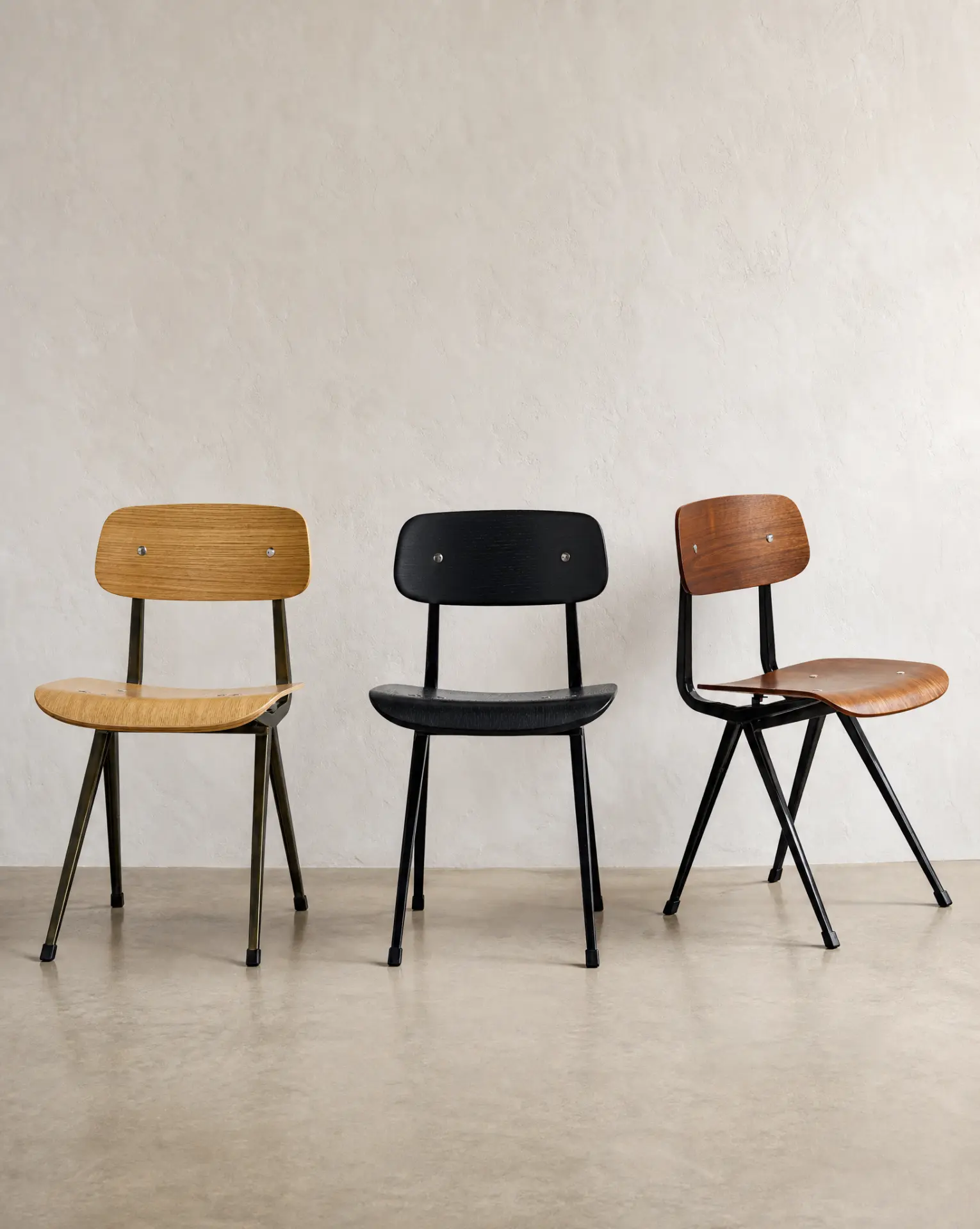 Three Madewell dining chairs — gunmetal steel with natural oak, black-on-black, and black steel with walnut plywood — against a soft plaster wall