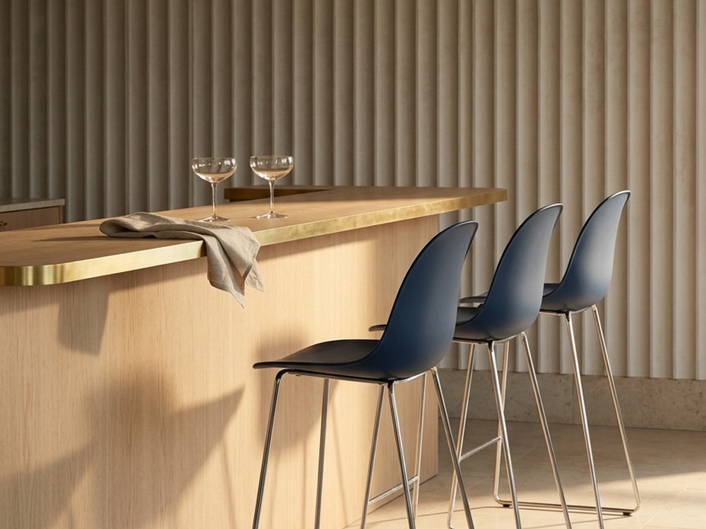 Navy Bell bar stools lined up at a light oak and brass hotel bar
